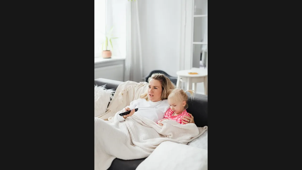 A woman holding a remote looks puzzled at the television while a young child sits beside her on the sofa