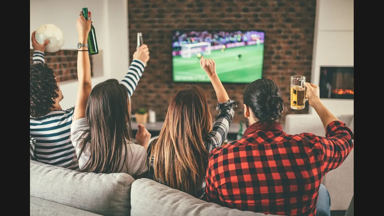 Friends on a sofa cheering with raised arms at a football match on a wall-mounted television