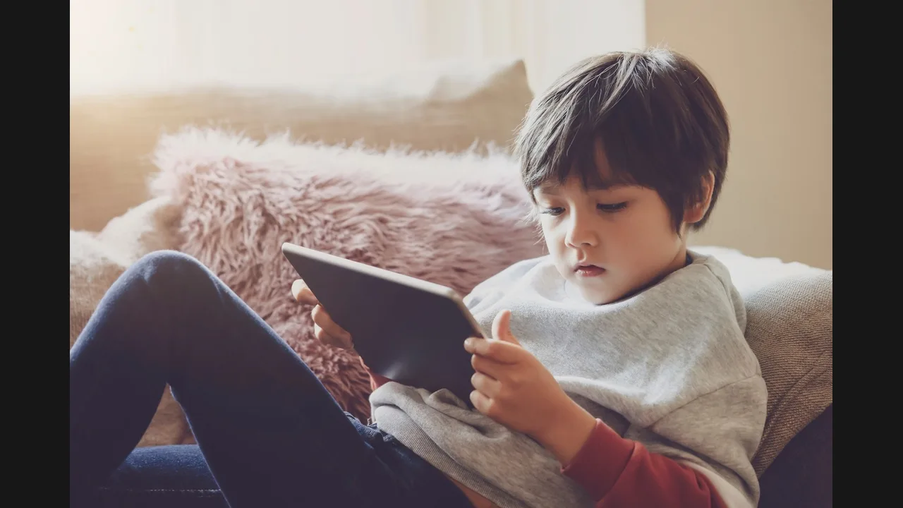 A young boy sitting on a sofa watching a tablet