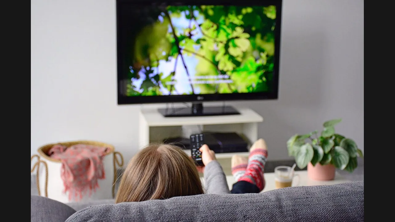 A viewer on a sofa watching a television that shows subtitles at the bottom of the screen
