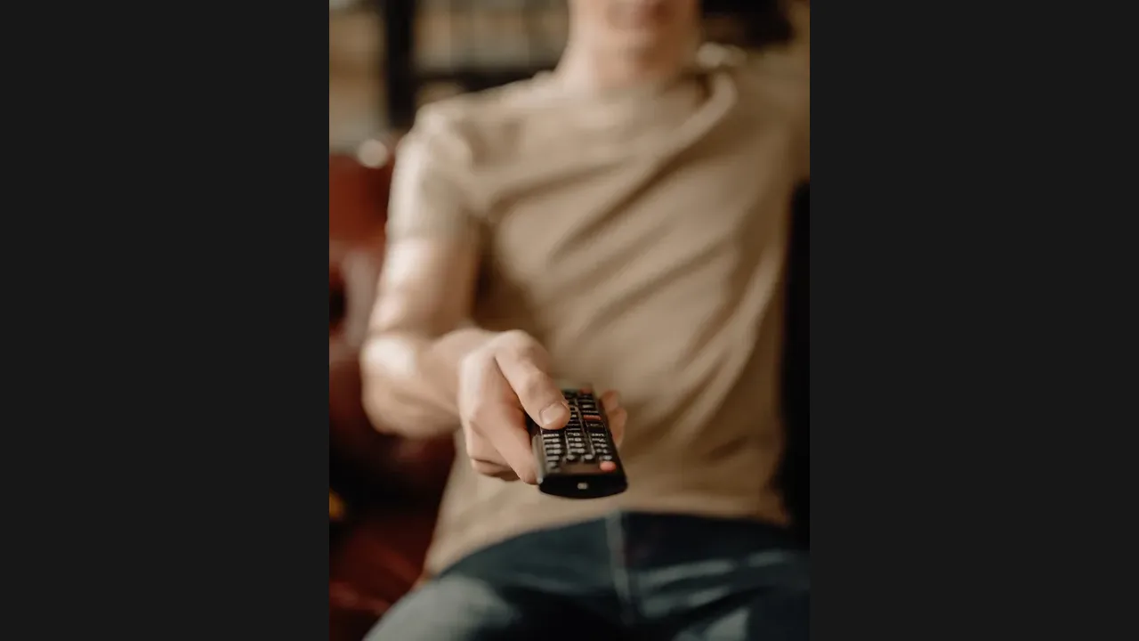 A person pointing a television remote control toward the television