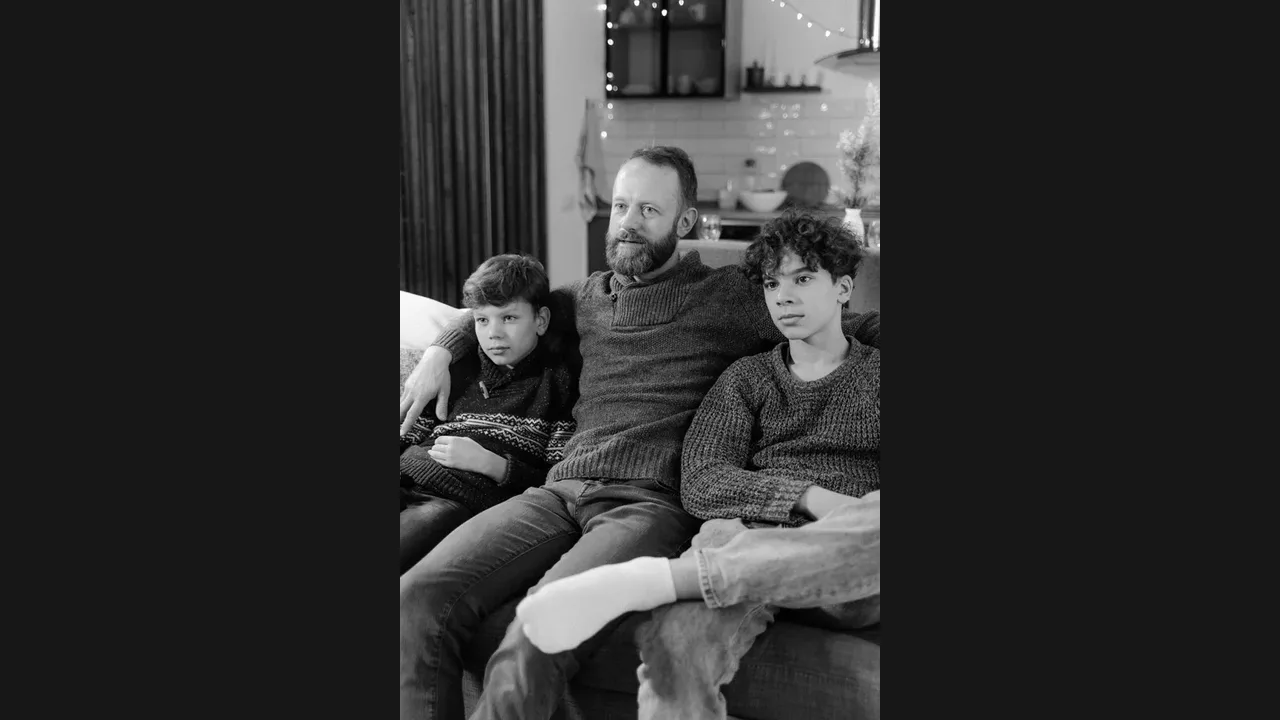 A father and his two sons sitting on a sofa watching television